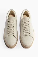 Zapatillas deportivas color crema de gamuza, con collarín acolchado, lengüeta y cierre de cordones. Forro y plantillas en lona de algodón. Suelas texturizadas con diseño.