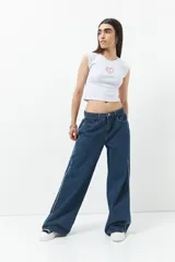 Pantalón de jean azul oscuro, corte ancho, tiro bajo y cinco bolsillos. Presenta una línea bordada blanca en ambas piernas.
