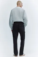 Pantalón cargo negro de corte slim fit, con cintura elástica y cordón ajustable. Presenta bolsillos al bies, bolsillos cargo en las piernas con solapa y botones a presión ocultos, y bolsillos traseros con solapa. Las piernas son ajustadas con costuras y pinzas en las rodillas.