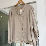 Camisa de lino color beige, con cuello mao, mangas largas abullonadas con puños elásticos y cierre frontal de botones.