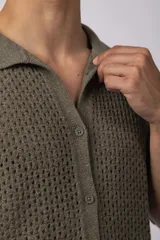 Camisa de punto calado en color beige, de manga corta y corte relajado. Presenta cuello tipo bowling, cierre frontal con botones al tono y una estructura liviana y respirable confeccionada en algodón.