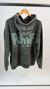 Canguro gris oscuro con efecto lavado, capucha con cordón ajustable y puños elásticos. Estampado en la espalda con la palabra "PEACE" en letras grandes color verde agua y símbolos relacionados con la paz.