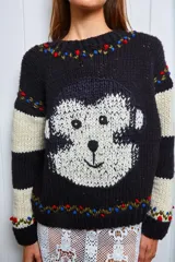 Sweater tejido de lana color negro con rayas horizontales color crema en las mangas y aplique de un mono tejido en el frente. Presenta detalles bordados en el cuello y los puños.