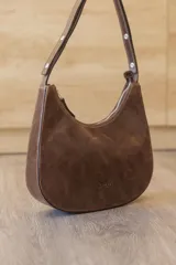 Cartera hobo de cuero color rojo con silueta curva de media luna, cierre superior y correa de hombro ajustable.