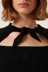 Suéter de punto negro con cuello anudado y abertura sobre el pecho. Presenta detalle de botones a presión con forma de sol en la parte delantera y bordado "TRS".