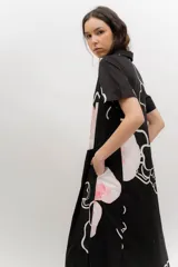 Vestido midi de popelina de algodón negra, con estampado floral en tonos rosados y blancos, cuello tipo bebe, mangas cortas, cierre frontal abotonado y bolsillos laterales.