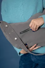 Bolso tipo bandolera de gamuza color marrón, con correa ancha ajustable decorada con tachas metálicas y cierre superior.