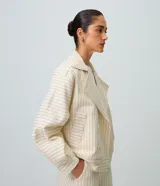 Tapado corto tipo trench coat confeccionado en sarga de algodón, de color beige con estampa de rayas finas verticales y horizontales. Presenta cuello solapa, mangas largas, bolsillos laterales con ribete y cierre frontal cruzado con doble botonadura.