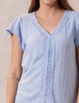 Blusa celeste en tejido pointelle con escote en V y mangas cortas con volados. Aplique de puntilla en el escote y en el frente.