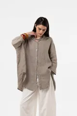 Camisa de lino de calce amplio y relajado, color beige, con cuello camisero, cierre frontal con botones y mangas largas.
