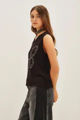 Musculosa negra con escote en V y aplique de mariposa hecho con tachas plateadas. Se complementa con un accesorio tipo choker/collar largo de cuentas plateadas.