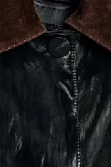 Trench de largo midi con acabado brillante efecto vinilo, manga larga y cuello de solapa en tejido de gamuza a contraste. Presenta cierre frontal con botones ocultos y bolsillos laterales integrados en la costura.