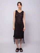 Vestido largo negro de tejido de punto con diseño de tramado y pequeños calados, sin mangas y con flecos en el ruedo.