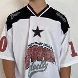 Camiseta estilo fútbol americano de corte oversize, color blanco con detalles en negro y rojo. Presenta estampado gráfico frontal con estrella y texto, además de números en las mangas.