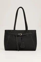 Cartera tipo shopper color marrón oscuro, con doble asa de hombro y detalles de costuras blancas a la vista. Cuenta con una tira decorativa con hebilla metálica dorada y un colgante tipo llavero al frente.
