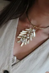 Gargantilla rígida dorada con dije colgante de forma irregular con incrustaciones de perlas y nácar.