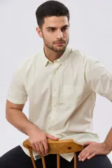 Camisa lisa de algodón azul marino, de manga corta, con cuello camisero, cierre frontal de botones y un bolsillo aplicado en el pecho.