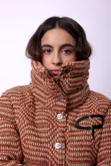 Campera corta con estampado abstracto en tonos marrones y beige, cuello alto, cierre frontal con botones a presión, bolsillos delanteros y bordado negro con las iniciales CP. Forro interior y relleno liviano de guata.