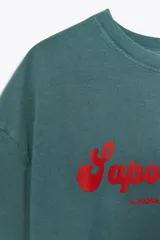 Camiseta de manga corta color verde azulado (teal) con efecto lavado, corte oversize y cuello redondo. Estampado frontal en color rojo con el texto "Sapore Felice" en tipografía cursiva.