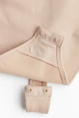 Body modelador tipo tanga color beige, con efecto vientre plano. Presenta copas forradas con sección en punto menguado para realce y sujeción suave, sin aros. Cuenta con breteles ajustables y cierre inferior con botones a presión ocultos. Diseño sin costuras para mayor comodidad.