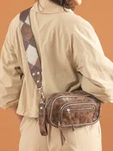 Riñonera de cuero vacuno con acabado texturado en tono marrón mocha, con herrajes plateados. Presenta un compartimento principal con cierre y un bolsillo frontal adicional con cierre. Incluye una correa ancha regulable con diseño geométrico de parches en tonos marrón y gris.