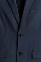 Blazer azul marino de corte slim fit, con solapas de muesca finas, botonadura sencilla de un botón visible, bolsillo superior insertado y dos bolsillos delanteros con solapa. Presenta abertura doble en la espalda y forro interior.