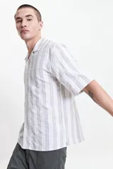 Camisa de manga corta a rayas verticales blancas y grises, con cuello camisero y corte recto. El modelo usa talle M.