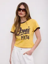 Remera amarilla de manga corta estilo ringer, con cuello y bordes de mangas en contraste color marrón oscuro. Presenta estampado frontal con la inscripción "Bowie 1974" y detalles de estrellas.