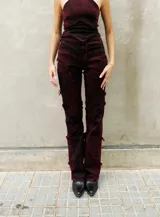 Pantalón de denim elastizado con efecto de lavado desgastado en tono bordó oscuro. Presenta un diseño de corte entallado con recortes irregulares, costuras expuestas con terminaciones desflecadas y tiro alto.