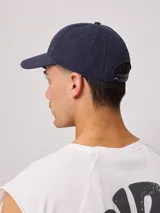 Gorro de visera estilo dad hat, color azul marino, confeccionado en lona lavada. Presenta un parche rectangular bordado en el frente con el logo de la marca Rusty.