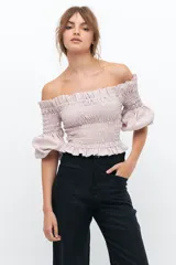 Crop top blanco con escote off-shoulder, punto panal en el torso y volados en el escote.
