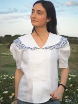 Blusa blanca de lino, de manga corta, con cuello marinero amplio decorado con estampado azul.