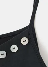 Top de tirantes finos color gris oscuro, con escote asimétrico decorado con detalles metálicos circulares en el borde.