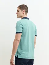 Remera manga corta color verde con cuello polo y bolsillo en el pecho. El cuello y los puños son de color azul marino.