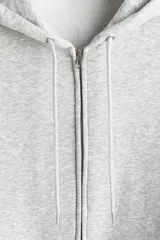 Campera con capucha de felpa gris melange, con cierre frontal, bolsillos tipo canguro y cordón ajustable. Presenta hombros caídos, corte holgado y puños y bajo en punto acanalado.