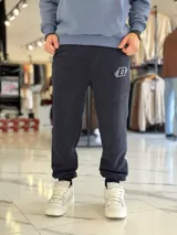 Pantalón jogger negro de corte oversize con felpa, bolsillos laterales y puños elásticos en los tobillos. Presenta un pequeño logo estampado en color blanco en la pierna izquierda.