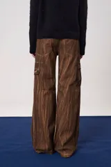 Pantalón cargo de tiro medio con pierna amplia, confeccionado en denim color marrón con efecto lavado. Presenta múltiples bolsillos laterales y frontales con solapa y cierre de botones.