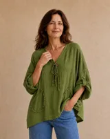Blusa verde de lino con escote en V, cordones ajustables con detalles de botones en el pecho, bolsillos frontales aplicados con bordes deshilachados y mangas 3/4 con tirilla y botón para arremangar.