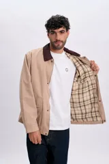 Campera color taupe con cuello de pana marrón oscuro, cierre frontal y botones a presión. Cuenta con dos bolsillos frontales con solapa.