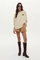 Buzo de felpa liviana color beige, con mangas largas, cuello redondo y bordado artesanal en el pecho.