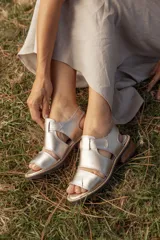 Sandalias de cuero natural metalizado color plateado, con tiras anchas, taco bajo de madera y tira con velcro para ajuste en el talón.
