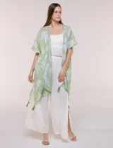 Kimono de gasa verde con estampado de hojas blancas y detalles de lurex. Presenta mangas cortas holgadas, diseño abierto al frente y terminación en punta con borlas en el ruedo.