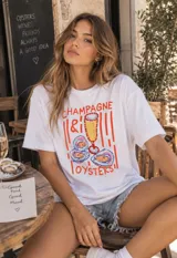 Remerón blanco de corte oversize con estampado frontal ilustrativo de champagne y ostras, acompañado de la frase 'CHAMPAGNE & OYSTERS'.