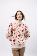 Polera de tejido de punto con cuello alto, diseño holgado y estampado jacquard con motivos geométricos y figuras en tonos beige, naranja y celeste.