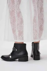 Botas cortas de cuero negro con tachas plateadas en la puntera y el talón, cierre lateral con cremallera y hebillas decorativas. Taco cuadrado bajo.