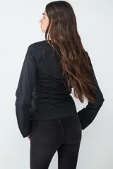 Blusa blanca de manga larga con escote redondo, cierre frontal oculto y detalles de frunces laterales en el cuerpo.