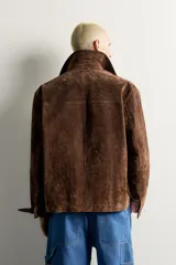 Parka de piel marrón tipo gamuza con cuello solapa, manga larga con puños de botones a presión y múltiples bolsillos de plastrón con solapa en el pecho y la cadera. Cierre frontal de cremallera oculta con solapa.