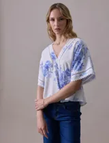 Blusa blanca estampada con flores azules, escote en V y mangas cortas amplias. Detalles de puntilla en escote y mangas.