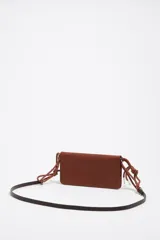 Minibolso negro de piel vacuna con textura granulada, formato rectangular y cierre de botón a presión. Incluye un tarjetero interior y dos asas: una de mano tipo cordón trenzado rojo y naranja, y una asa larga extraíble.