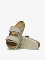 Sandalia Birkenstock modelo Uji en color taupe, confeccionada con una parte superior de gamuza suave y correas de nobuk con cierre de velcro. Presenta la clásica plantilla anatómica de corcho y suela de EVA.